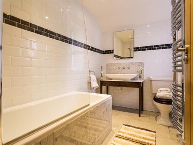 A bathroom with a bathtub a sink on a wooden vanity a toilet and a striped rug at Oaklea Ambleside