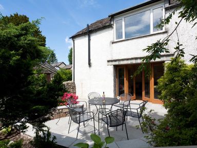 An outdoor patio area with a round table and six metal chairs near a white house at Oaklea in Ambleside