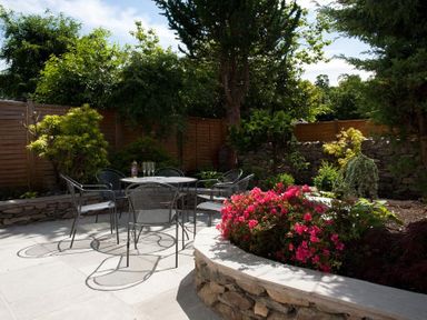 An outdoor patio area with metal chairs and table surrounded by plants and trees at Oaklea in Ambleside