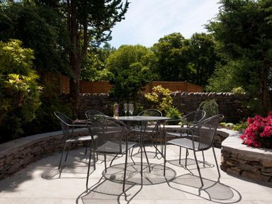 An outdoor patio with a round metal table and six chairs surrounded by stone walls and plants at Oaklea in Ambleside