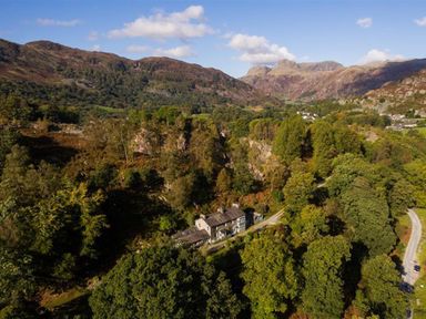 A house surrounded by trees with mountains in the background at Oakbank in Langdale