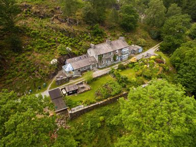 An aerial view of a stone house with a garden and surrounding trees at Oakbank in Langdale