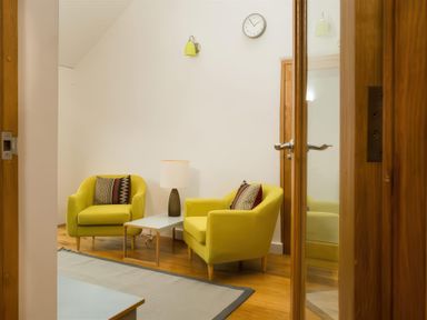 A room with two yellow armchairs a small table with a lamp a wall clock and a wooden floor at Oakbank Langdale