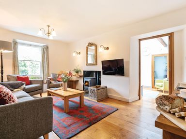 A living room with grey sofas a wooden coffee table a red and blue rug a wood burning stove and a wall-mounted TV at Oakbank in Langdale