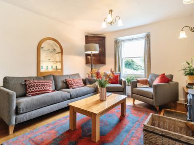 A living room with gray sofas red pillows a wooden coffee table with flowers and a red and blue rug at Oakbank in Langdale