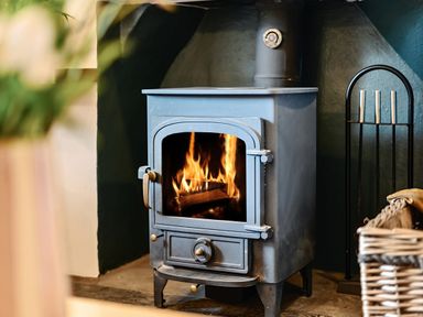 A burning wood stove in a fireplace with a basket and fireplace tools nearby at Oakbank in Langdale