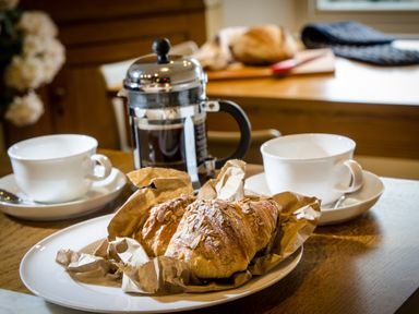 Two croissants on a plate with brown paper next to two empty white cups and a French press coffee maker on a wooden table at Oakbank in Langdale