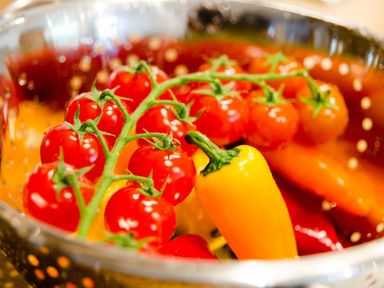 Red cherry tomatoes on the vine with a yellow pepper in a metal colander