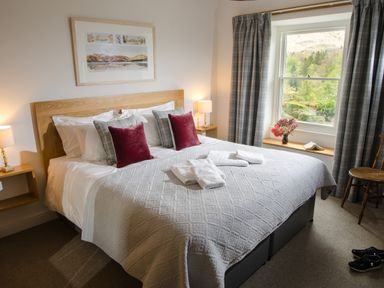 A bedroom with a large bed with pillows and folded towels beside a window with curtains and a chair at Oakbank in Langdale