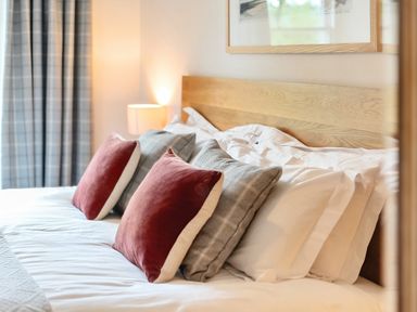 A bed with multiple pillows and cushions next to a lamp and curtains at Oakbank in Langdale