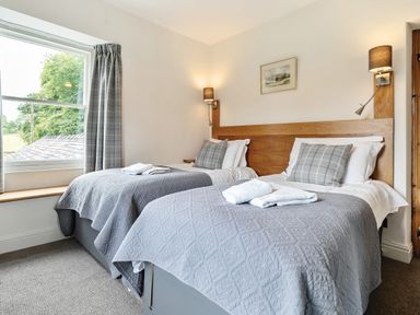 A bedroom with two single beds gray bedding and pillows a window with gray curtains and two wall lamps at Oakbank in Langdale