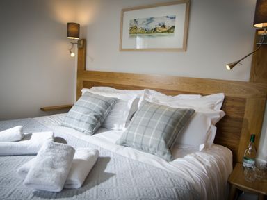 A bed with gray pillows and folded white towels on a patterned blanket with wall lamps and a framed landscape picture at Oakbank in Langdale