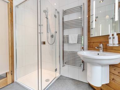 A bathroom with a glass shower enclosure a white sink a wall-mounted mirror and a chrome towel radiator at Oakbank Langdale