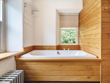 A bathroom with a bathtub surrounded by wood paneling and a window with a roller blind at Oakbank in Langdale