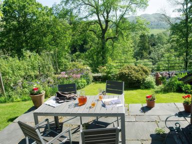 A garden patio with a table and four chairs surrounded by plants and trees at Oakbank in Langdale