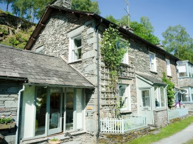 A stone cottage with windows and a small garden fence at Oakbank in Langdale