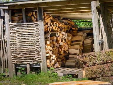 A wood storage shed with logs stacked on pallets and wooden branches at Oakbank in Langdale