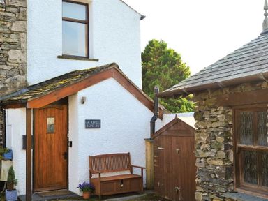 The entrance of a white house with a wooden door a bench and stone outbuilding at A River Runs By in Staveley