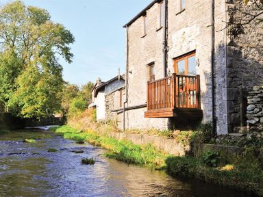 A stone building with a wooden balcony overlooking a river with trees nearby at A River Runs By in Staveley