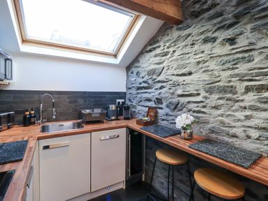 A kitchen with wooden countertops a stone wall two stools and a skylight window at Workshop Cottage in Bowness