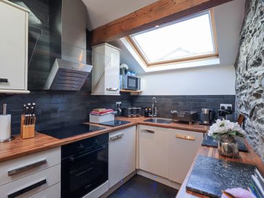 A kitchen with wooden countertops white cabinets a skylight and stone wall at Workshop Cottage in Bowness