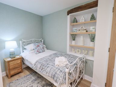 A bedroom with a single bed white metal frame bedside table with lamp shelves with decorations at Workshop Cottage in Bowness