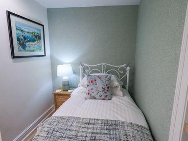 A small bedroom with a single bed a wooden bedside table with a lamp and a framed picture on the wall at Workshop Cottage in Bowness
