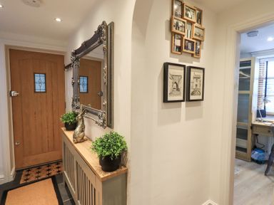 A hallway with a wooden door a console table with plants and a decorative rabbit and a mirror above at Workshop Cottage in Bowness