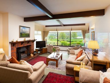 A living room with sofas a coffee table a fireplace and large windows overlooking a garden at Lakefield House in Hawkshead