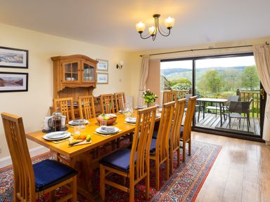 A dining room with wooden table and chairs set with plates and fruit and sliding glass door opening to outdoor seating at Lakefield House in Hawkshead