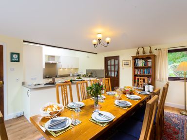 A dining room with a wooden table set for a meal next to a kitchen and bookshelf at Lakefield House in Hawkshead