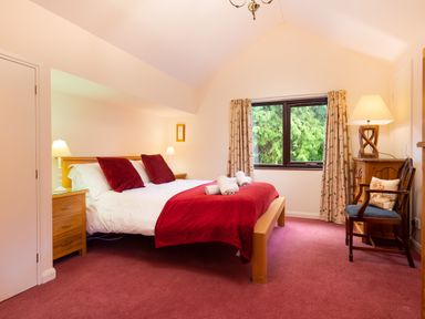 A bedroom with a bed with red pillows and blanket beside two bedside tables with lamps and a window with curtains at Lakefield House in Hawkshead