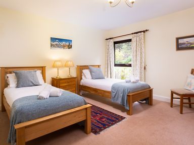 A bedroom with two single beds a wooden nightstand with lamps and a window with curtains at Lakefield House in Hawkshead
