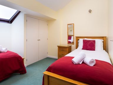 A bedroom with two single beds red bedding white towels and a wooden nightstand at Lakefield House in Hawkshead
