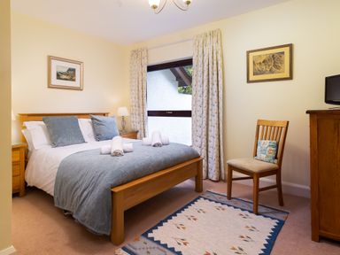 A bedroom with a wooden bed with folded towels on the bed two paintings on walls a wooden chair with a cushion a wooden dresser and a rug on the floor at Lakefield House in Hawkshead