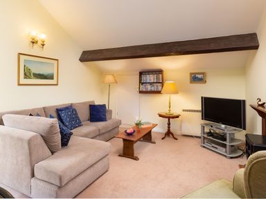 A living room with a beige sofa and blue cushions a wooden coffee table a flat screen tv on a stand and a floor lamp at Lakefield House in Hawkshead