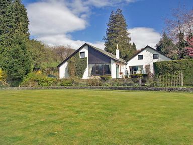 A house with a large lawn and various trees and shrubs around it at Lakefield House in Hawkshead