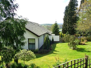 A garden with grass, trees, and shrubs around a white house at Lakefield House in Hawkshead