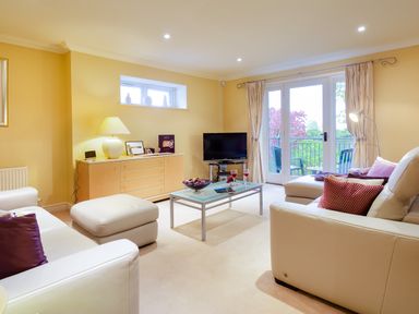 A living room with white sofas a glass coffee table and a TV near a balcony at Merewood Lodge in Ambleside