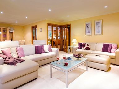 A living room with beige sofas, purple cushions, a glass coffee table with two glasses and a bowl, and a dining area with wooden furniture at Merewood Lodge in Ambleside