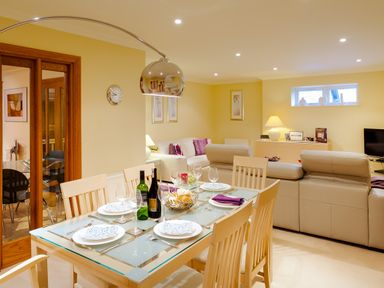 A dining table set with plates glasses and bottles next to a living area with sofas and a television at Merewood Lodge in Ambleside