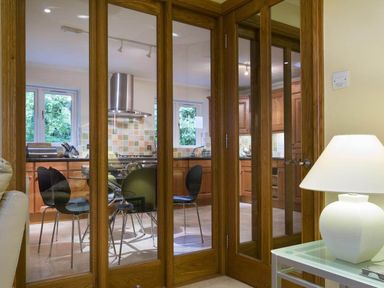 A kitchen with wooden cabinets and a glass dining table with black chairs seen through wooden framed glass doors at Merewood Lodge in Ambleside