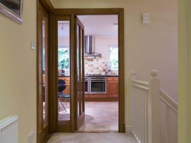 View through wooden framed glass doors into a kitchen with tiled backsplash and stainless steel oven at Merewood Lodge in Ambleside