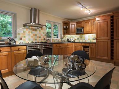 A kitchen with wooden cabinets tiled backsplash and a glass round dining table with tea set at Merewood Lodge in Ambleside