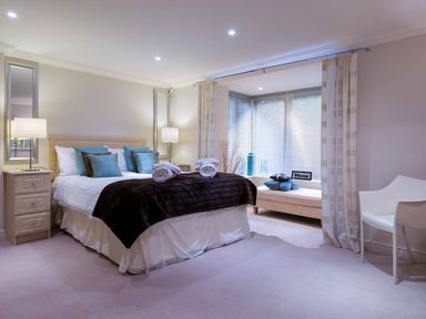 A bedroom with a double bed pillows and rolled towels bedside tables lamps mirrors window bench with cushions and a chair at Merewood Lodge in Ambleside