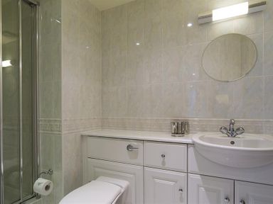A bathroom with a toilet a sink a round mirror and a shower enclosure at Merewood Lodge in Ambleside