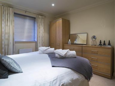 A bedroom with a bed with pillows and towels a wooden wardrobe and a wooden dresser with a mirror at Merewood Lodge in Ambleside