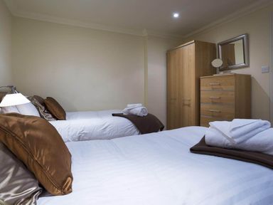 A bedroom with two beds brown pillows wooden wardrobe and dresser with mirror at Merewood Lodge in Ambleside