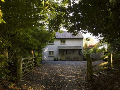 A two-story house with a gravel driveway and wooden gates surrounded by trees at Merewood Lodge in Ambleside