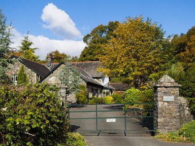 A stone house with a green metal gate and trees at Merewood Lodge in Ambleside